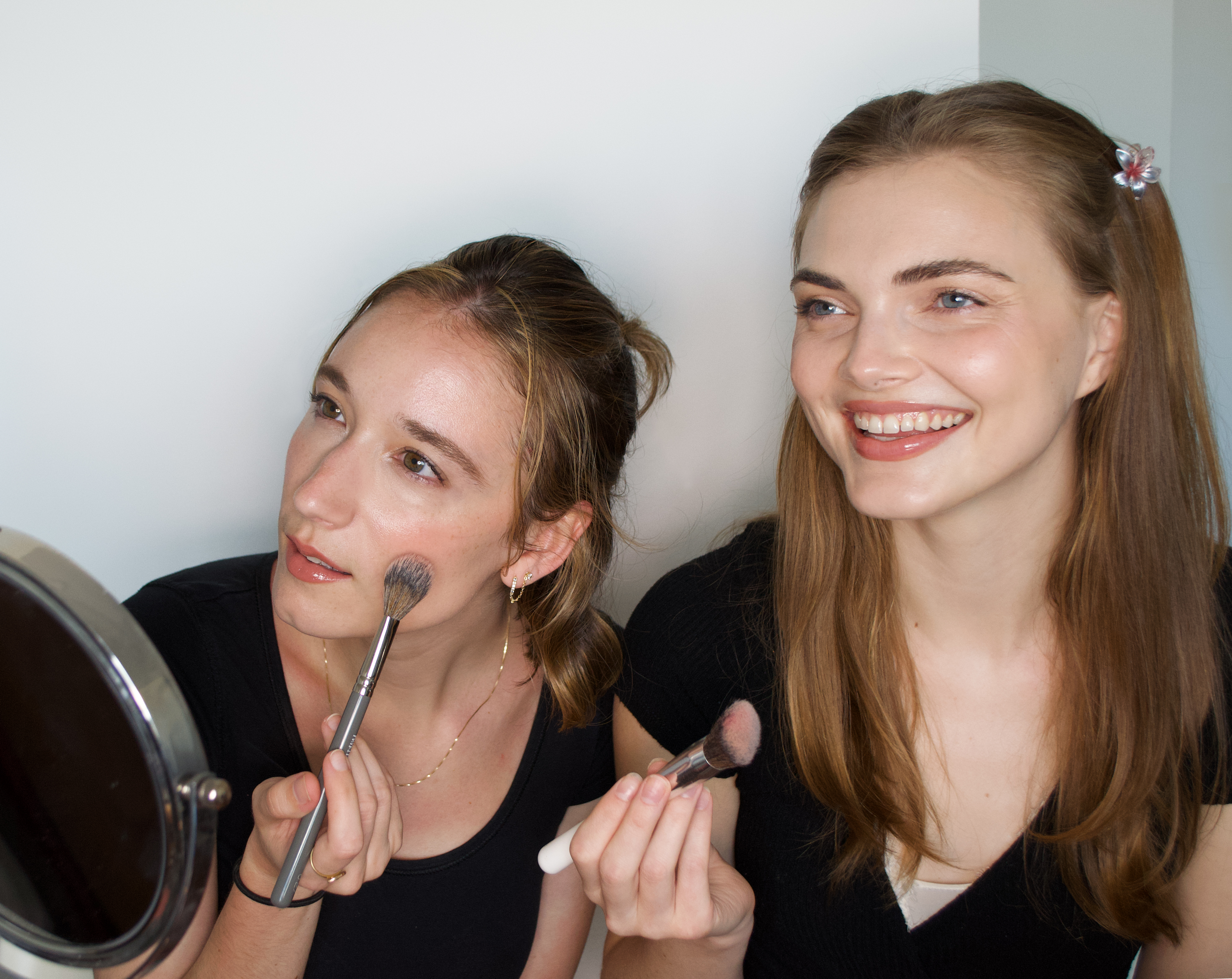 two women applying makeup in front of a mirror